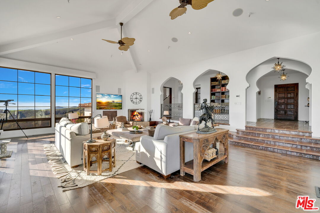 9785 Deer Creek Road Malibu, CA 90265 - Photo 9 of 75 a living room with couches a fireplace and kitchen view with wooden floor
