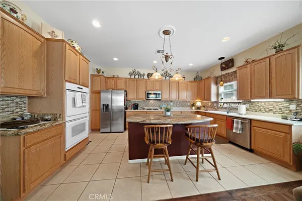a kitchen with stainless steel appliances granite countertop a sink a stove a refrigerator cabinets and chairs
