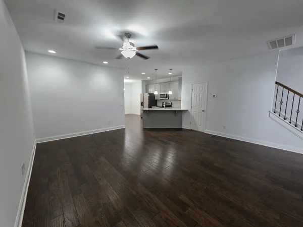 an empty room with wooden floor chandelier fan and kitchen view