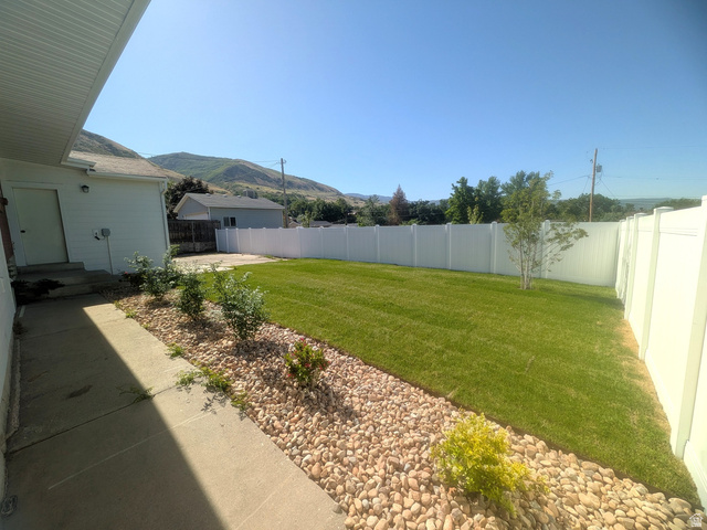 360 400 North Centerville, UT 84014 - Photo 7 of 30 Expansive backyard featuring a lush lawn, white vinyl fencing, and a decorative rock border with plantings