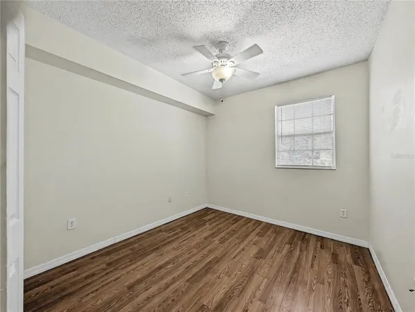 an empty room with wooden floor chandelier fan and windows