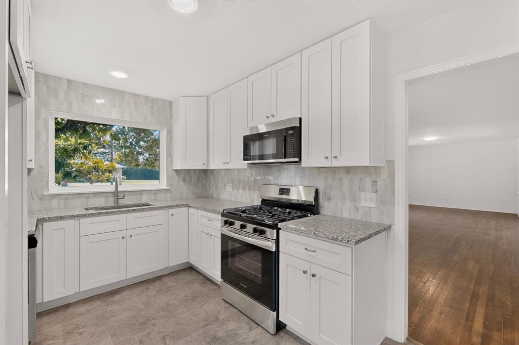 Corner kitchen featuring white shaker cabinetry, stainless steel appliances, speckled stone countertops, and a full-height tile backsplash