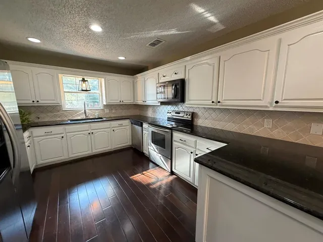 a kitchen with granite countertop a sink a counter top space stainless steel appliances and cabinets