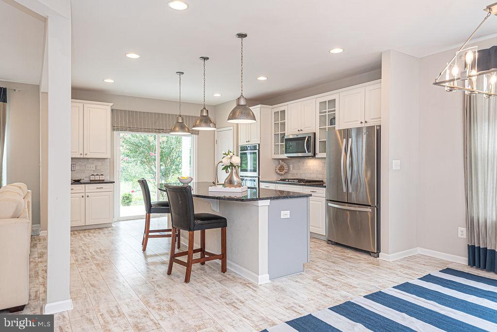 30134 Islander Beach Road Frankford, DE 19945 - Photo 15 of 73 a kitchen with stainless steel appliances granite countertop a refrigerator a sink dishwasher a stove a dining table and chairs with wooden floor