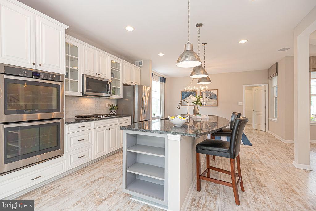 30134 Islander Beach Road Frankford, DE 19945 - Photo 23 of 73 a kitchen with stainless steel appliances granite countertop a stove top oven a sink dishwasher a dining table and chairs with wooden floor