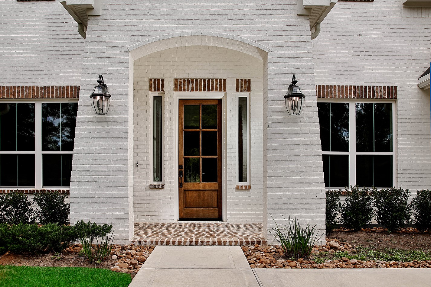 11709 Grand N Road Willis, TX 77378 - Photo 3 of 37 Pristine architectural details highlight front entrance with arched white brick opening, accented by antique brick on window headers/sills, porch decking, and the rich-wood stained custom door with 6-lites welcomes you inside.