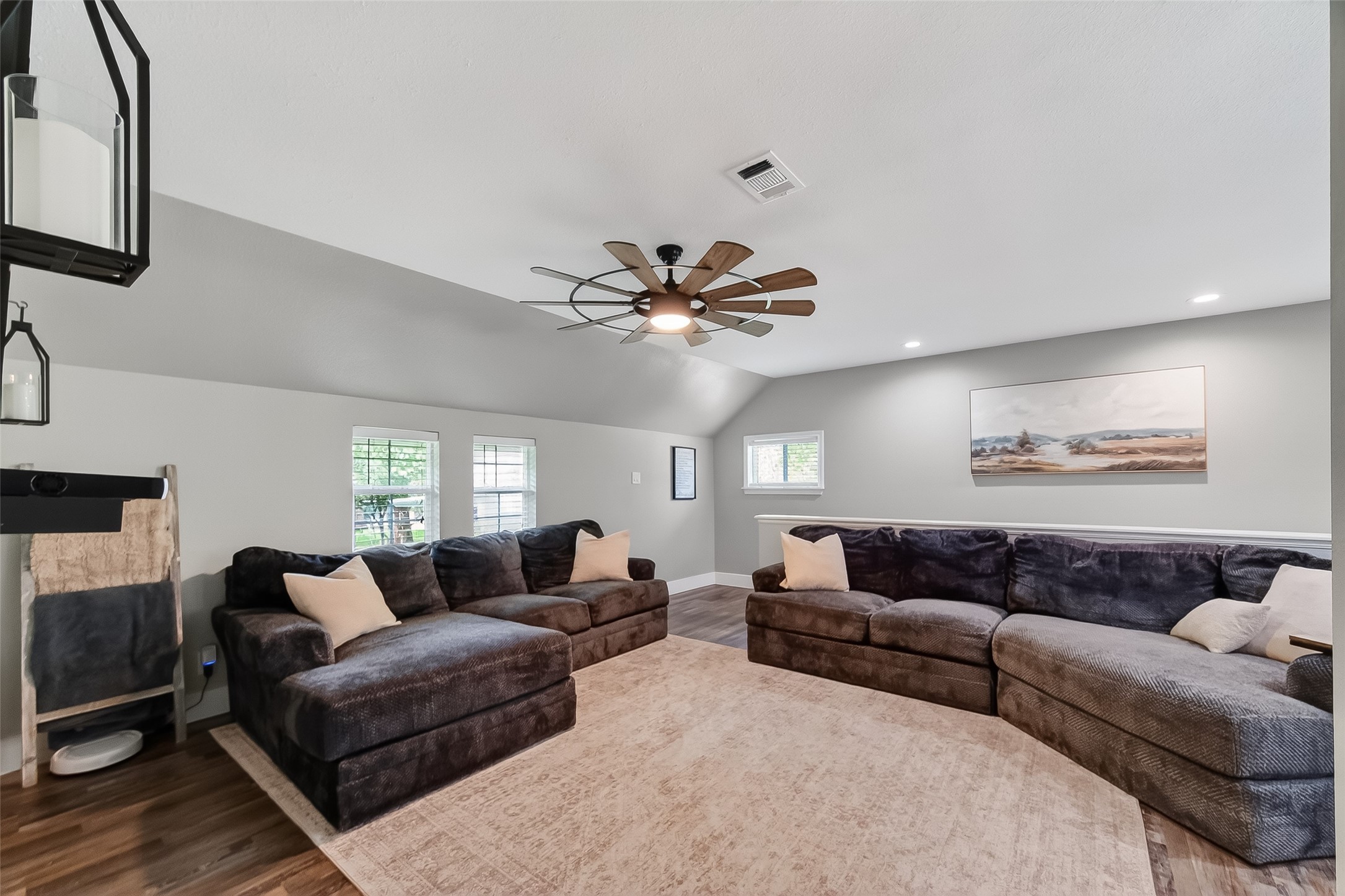 819 Sentinel Oaks Pinehurst, TX 77362 - Photo 11 of 38 This spacious living room features a large sectional sofa, a ceiling fan with a unique design, and ample natural light from multiple windows. The room is accented with a neutral color palette, a soft area rug, and modern wall art, creating a cozy and inviting atmosphere.