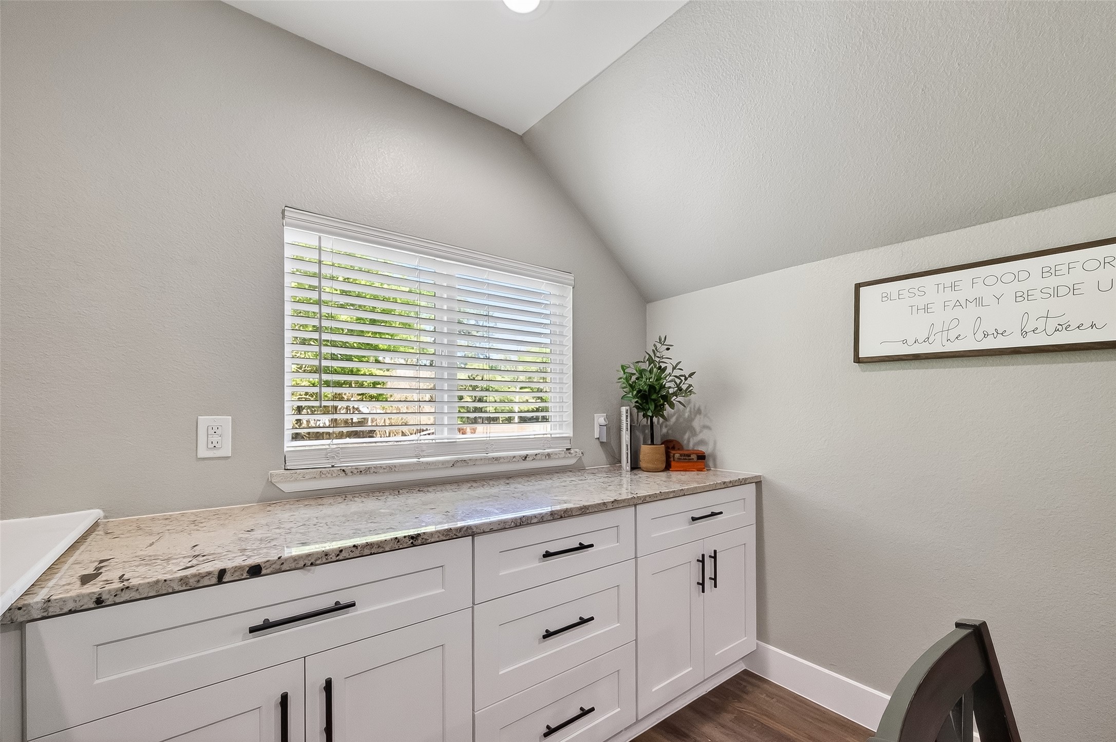 819 Sentinel Oaks Pinehurst, TX 77362 - Photo 16 of 38 This photo showcases a bright, cozy nook with a granite countertop, white cabinetry, and a window with blinds offering natural light. The space is decorated with a small plant and a sign, creating a welcoming atmosphere. Ideal for a desk or small workspace.