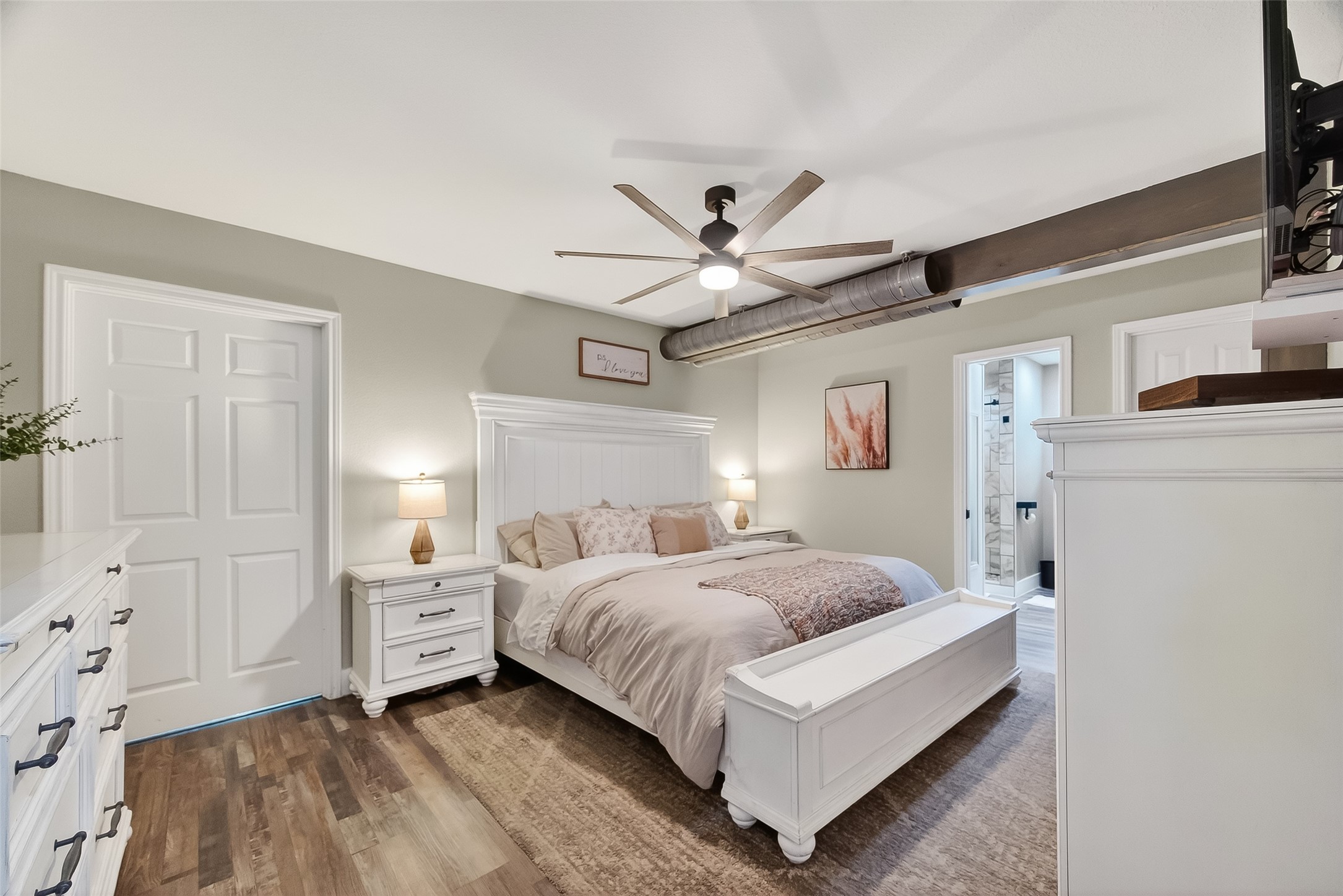 819 Sentinel Oaks Pinehurst, TX 77362 - Photo 20 of 38 This cozy bedroom features a modern ceiling fan, elegant wood flooring, and a neutral color palette. It includes a large bed with matching white furniture, creating a serene and inviting atmosphere. An en-suite bathroom and ample closet space add functionality.