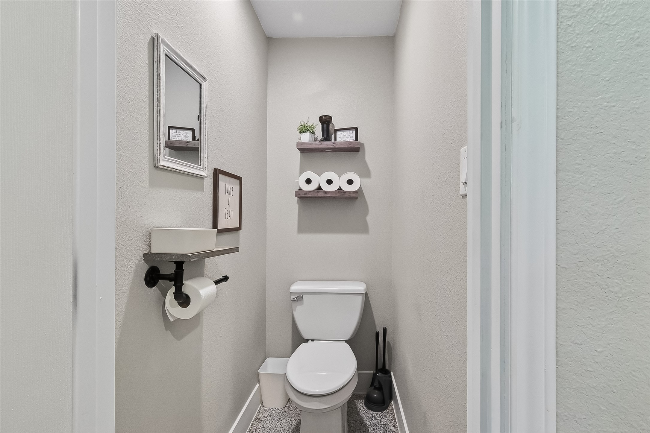 819 Sentinel Oaks Pinehurst, TX 77362 - Photo 32 of 38 This is a compact, well-organized powder room with a modern toilet and a small wall-mounted sink. It features neutral-colored walls, a decorative shelf with essentials, and a soft, patterned floor.