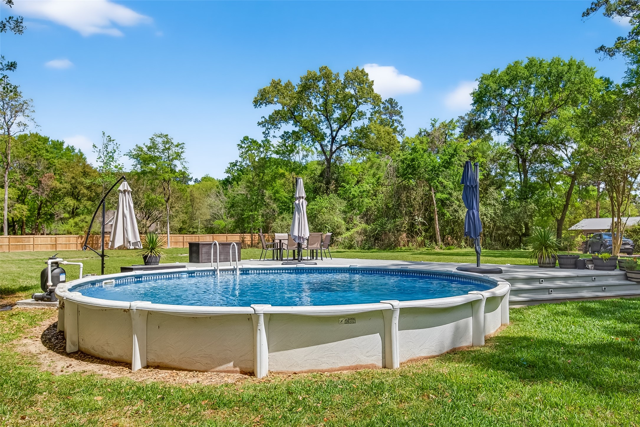 819 Sentinel Oaks Pinehurst, TX 77362 - Photo 33 of 38 This backyard features a spacious above-ground pool surrounded by lush greenery, perfect for outdoor relaxation and entertainment. The area includes a deck with seating and umbrellas, offering a serene retreat.