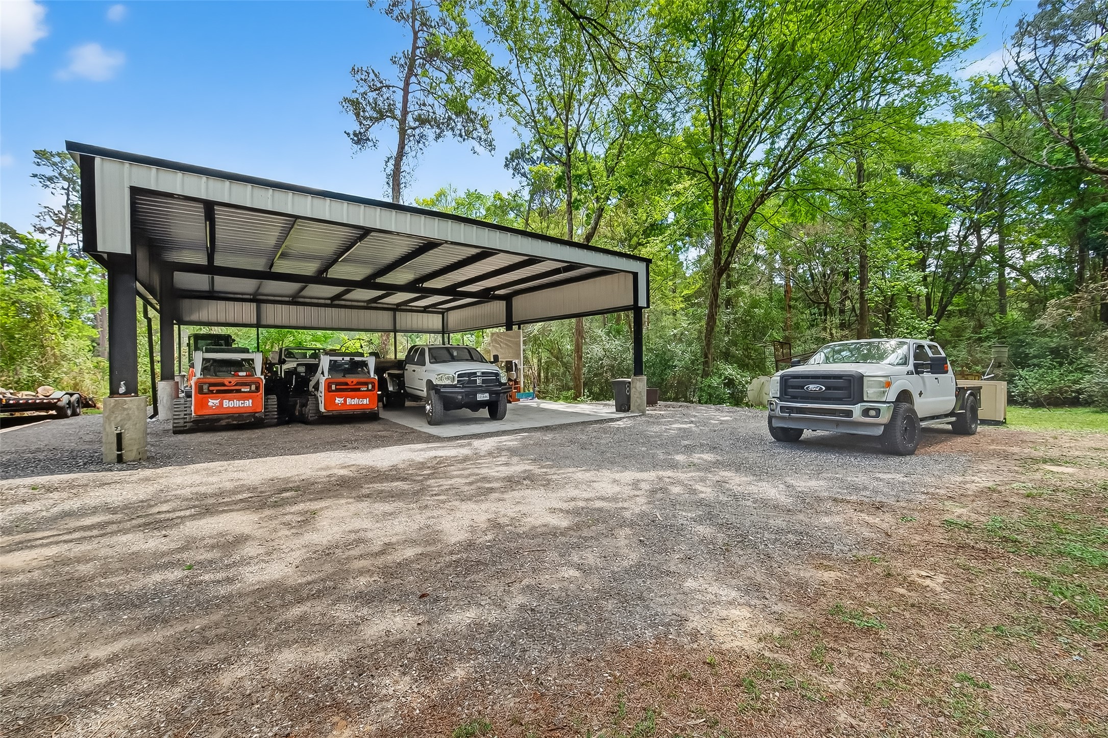 819 Sentinel Oaks Pinehurst, TX 77362 - Photo 35 of 38 This photo showcases a spacious outdoor area with a large, metal carport sheltering several vehicles, surrounded by a wooded landscape. Ideal for vehicle protection and storage, the setting offers privacy and a natural environment.