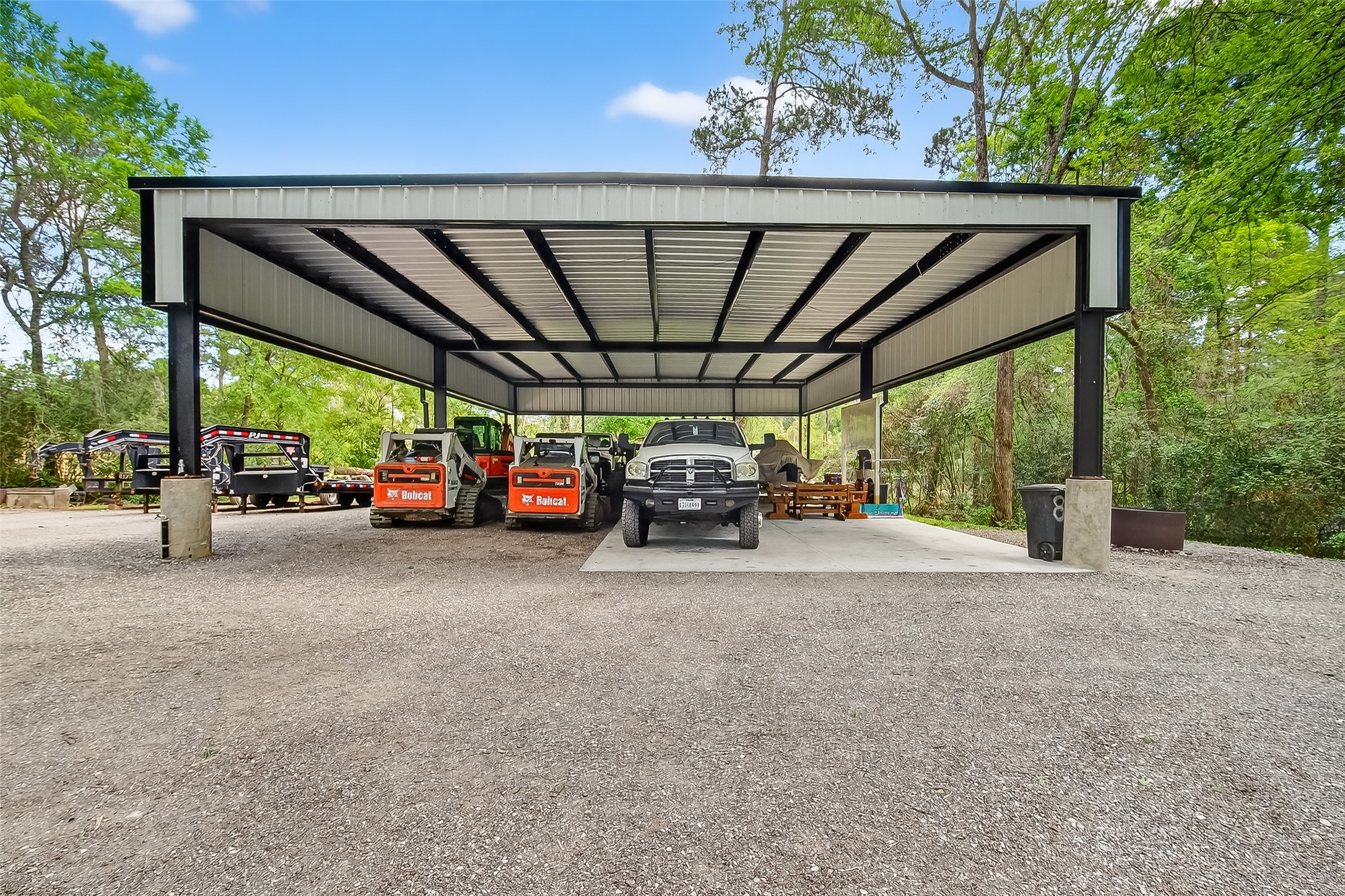 819 Sentinel Oaks Pinehurst, TX 77362 - Photo 36 of 38 This photo features a spacious metal carport with ample room for vehicles and equipment, set against a backdrop of lush greenery. Ideal for outdoor storage or workshop use.