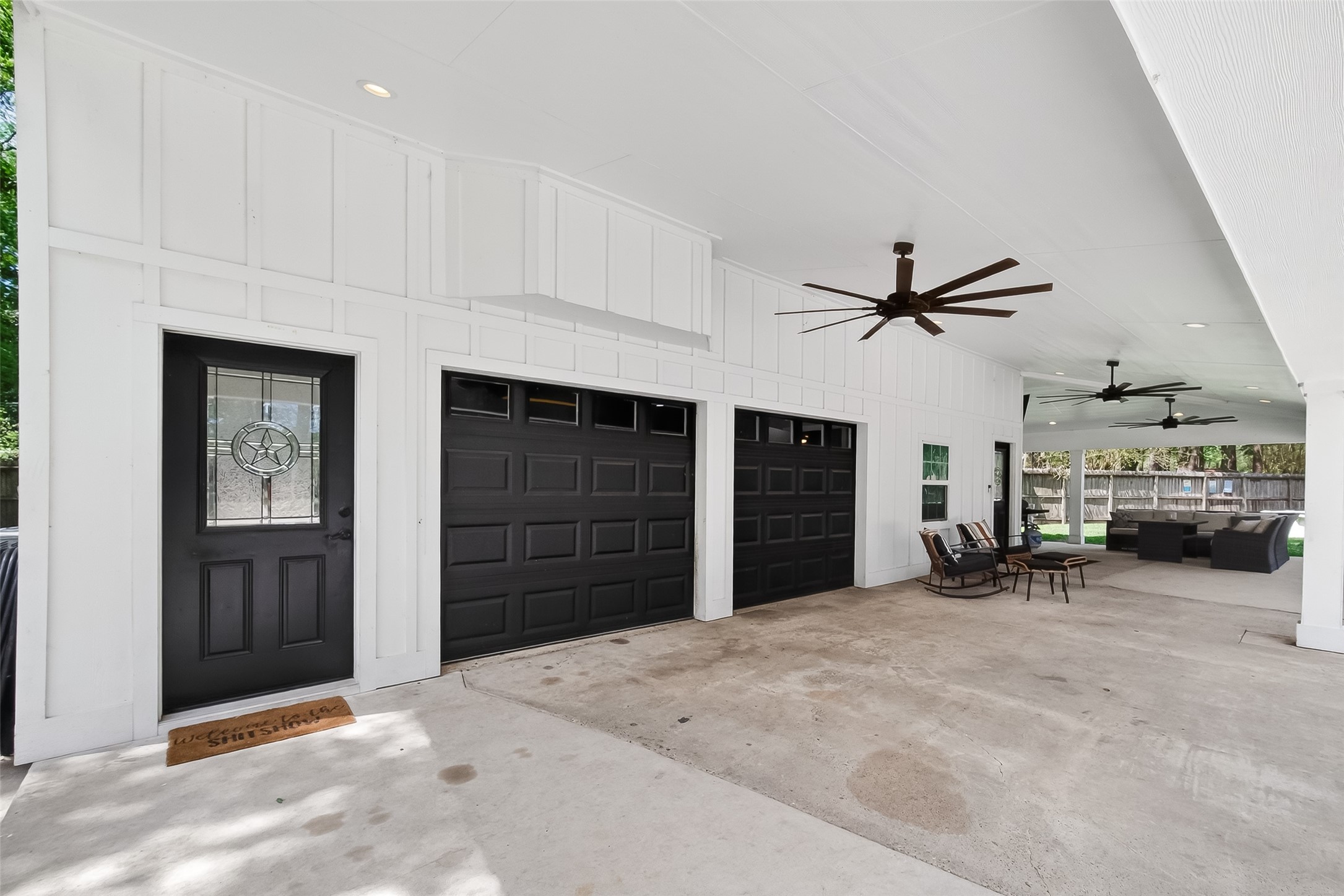819 Sentinel Oaks Pinehurst, TX 77362 - Photo 9 of 38 This spacious, covered patio features a white exterior with black garage doors and an elegant entry door. It includes ceiling fans for comfort and offers a cozy seating area, leading to a well-maintained backyard.
