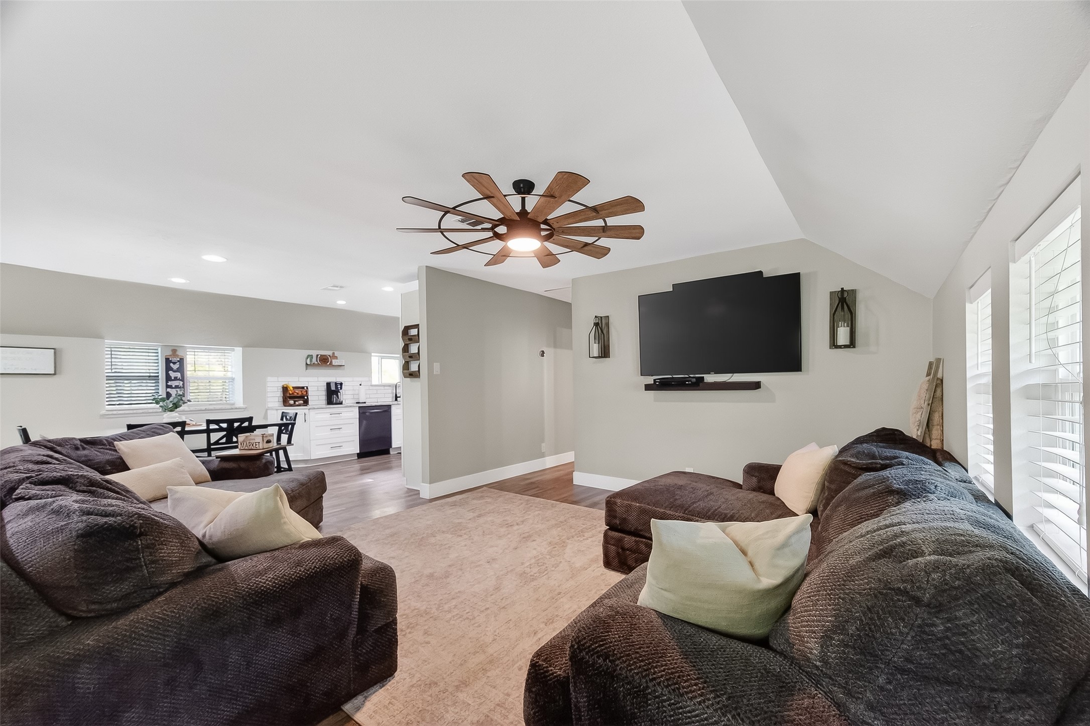 819 Sentinel Oaks Pinehurst, TX 77362 - Photo 10 of 38 This inviting living room features cozy dark sofas, a modern ceiling fan, and a wall-mounted TV. The open layout leads into a dining area and kitchen with ample natural light from large windows.