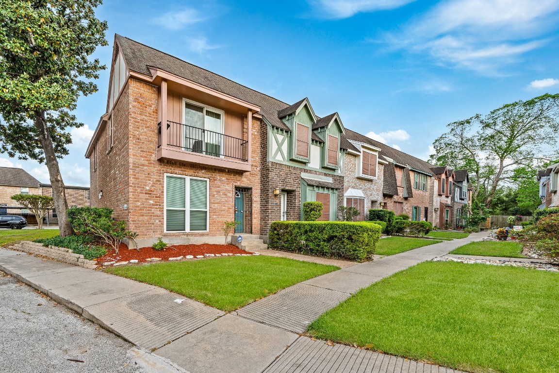 Charming brick townhouse with manicured lawns and a tidy sidewalk. The exterior features a mix of brick and siding, with neatly trimmed hedges and a small front garden. A quiet, tree-lined street enhances the inviting curb appeal.