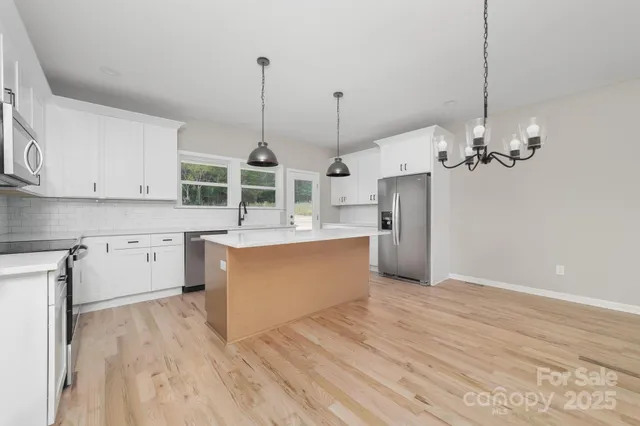 a large kitchen with stainless steel appliances granite countertop a stove a sink dishwasher a refrigerator and white cabinets with wooden floor