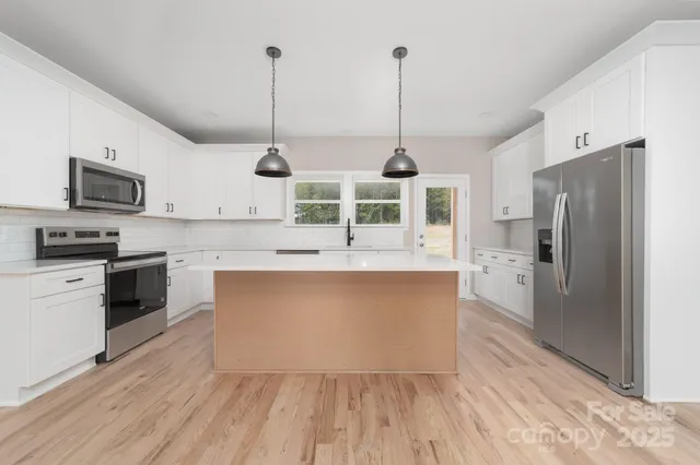 a kitchen with stainless steel appliances granite countertop a refrigerator a stove a sink and a wooden floor