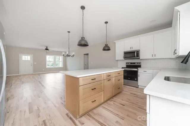 a kitchen with stainless steel appliances kitchen island granite countertop a sink a stove and white cabinets with wooden floor