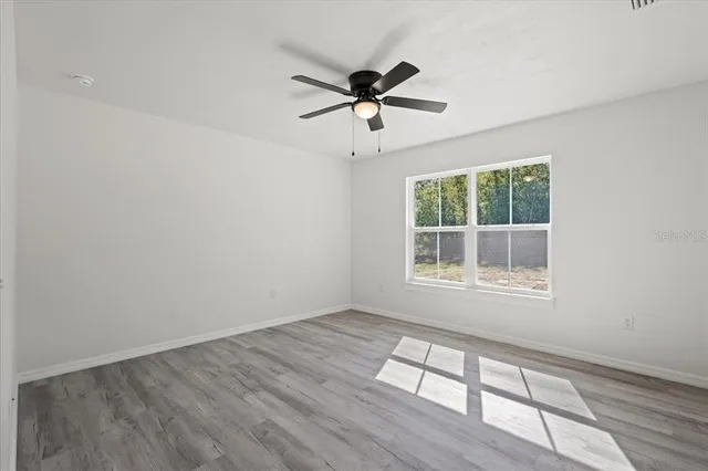 an empty room with wooden floor fan and windows