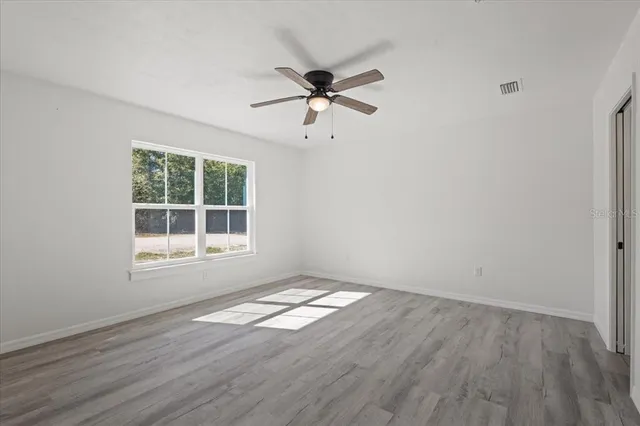an empty room with wooden floor fan and windows
