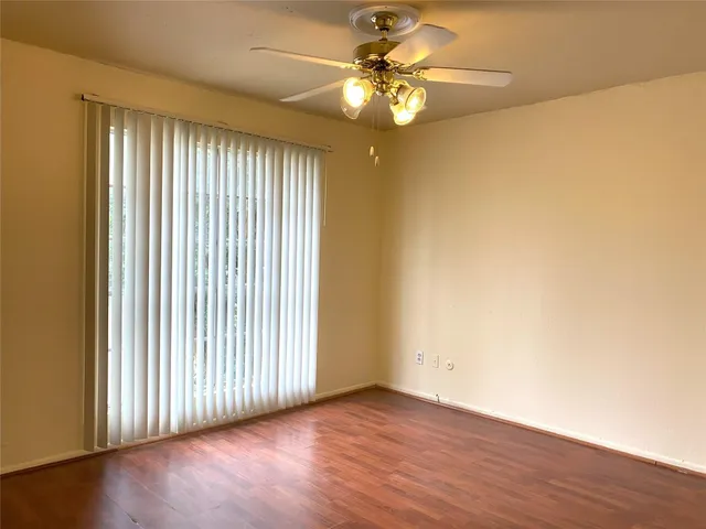 an empty room with wooden floor fan and windows