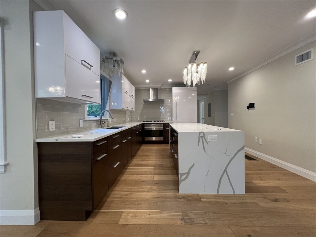 23 Winslow Road, Unit 1 Brookline, MA 02446 - Photo 5 of 27 a large kitchen with kitchen island a sink dishwasher a stove and a dining table with wooden floor