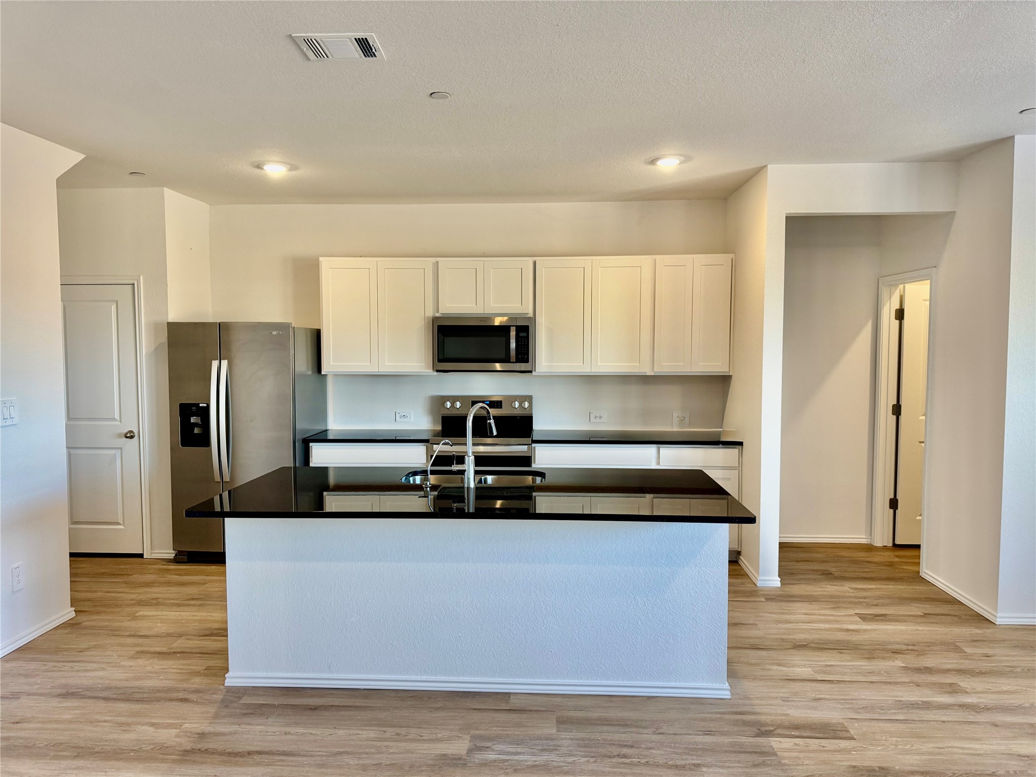 104 Calcite Road, Unit 2 Kyle, TX 78640 - Photo 2 of 21 Kitchen featuring appliances with stainless steel finishes, white cabinetry, light wood-style floors, a center island with sink, and dark stone countertops