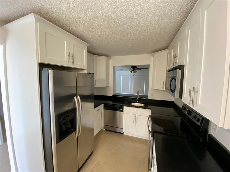 23466 Southwest 57th Avenue, Unit 504 Boca Raton, FL 33428 - Photo 2 of 20 a kitchen with a sink a refrigerator and cabinets