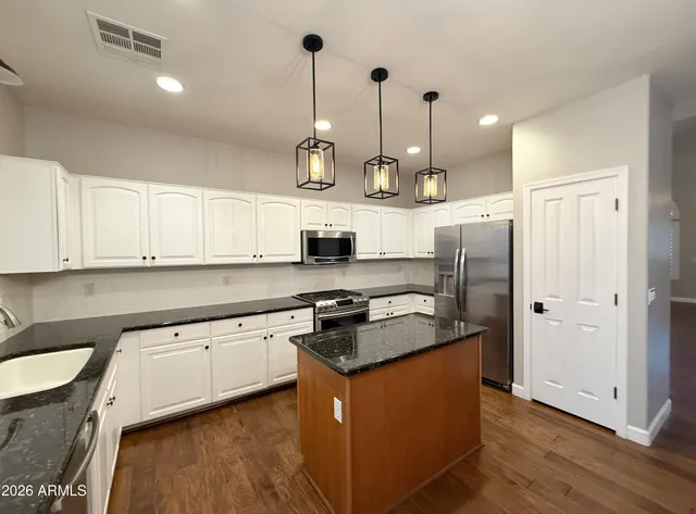 an empty room with wooden floor a ceiling fan and kitchen view