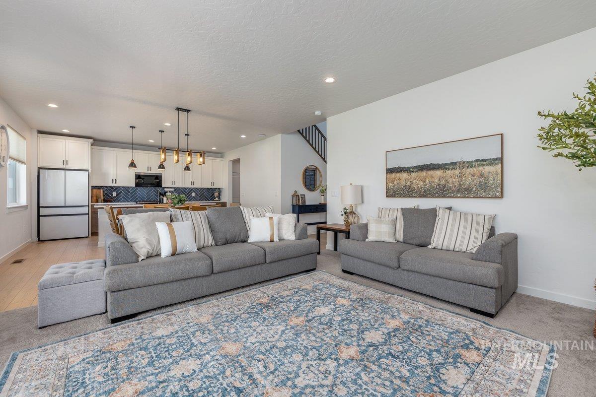 1380 West Chilitna Street Meridian, ID 83642 - Photo 21 of 50 Open-concept living area featuring a kitchen with white cabinetry and a chevron tile backsplash, a large kitchen island with seating, recessed lighting, and wood-finish flooring extending into the kitchen space