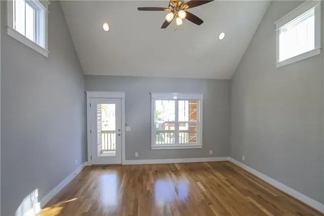 an empty room with wooden floor chandelier fan and windows