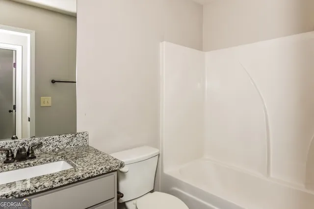 a bathroom with a granite countertop sink a toilet a mirror and shower