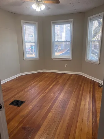 a view of an empty room with wooden floor and a window