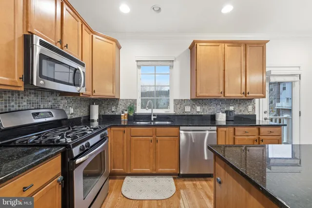 a kitchen with stainless steel appliances granite countertop a refrigerator a stove a sink dishwasher a dining table and chairs with wooden floor