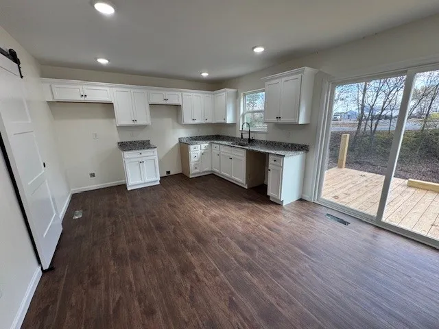 a large kitchen with stainless steel appliances granite countertop a stove a sink dishwasher a refrigerator white cabinets and wooden floor