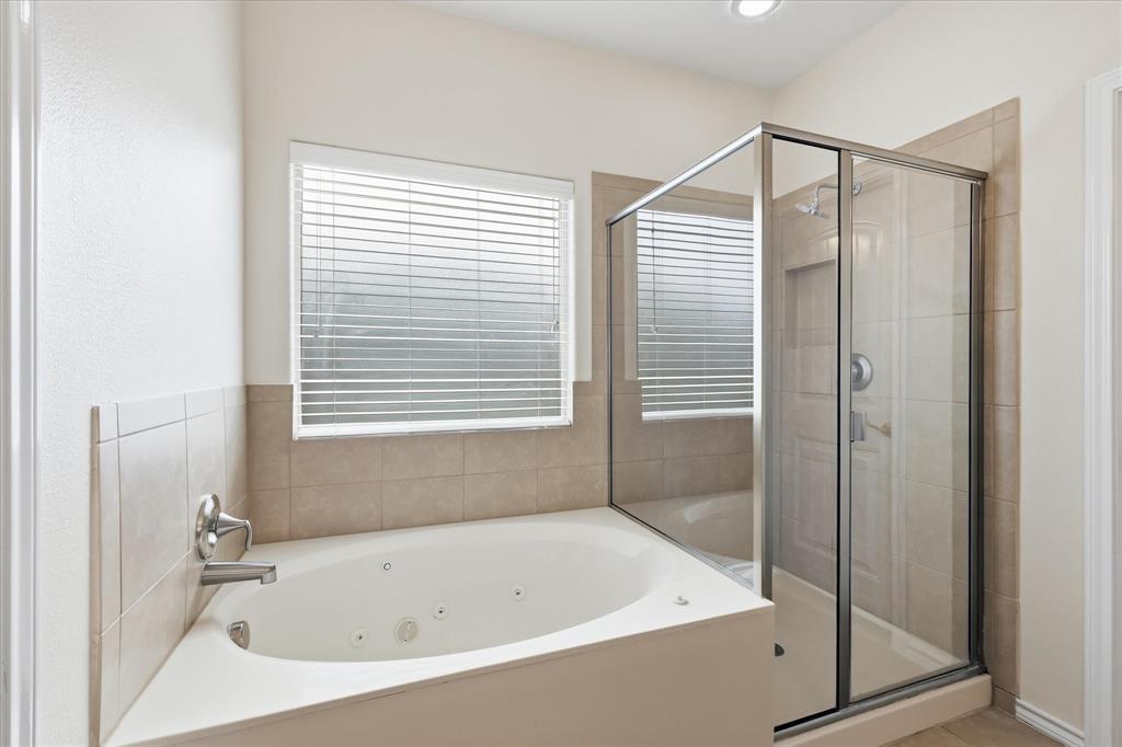 720 Rio Bravo Drive Fort Worth, TX 76052 - Photo 24 of 38 Bathroom featuring a built-in jetted tub, a glass-enclosed shower, neutral tile surround, and a window with blinds