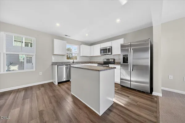 a kitchen with stainless steel appliances granite countertop a refrigerator oven a sink and white cabinets with wooden floor