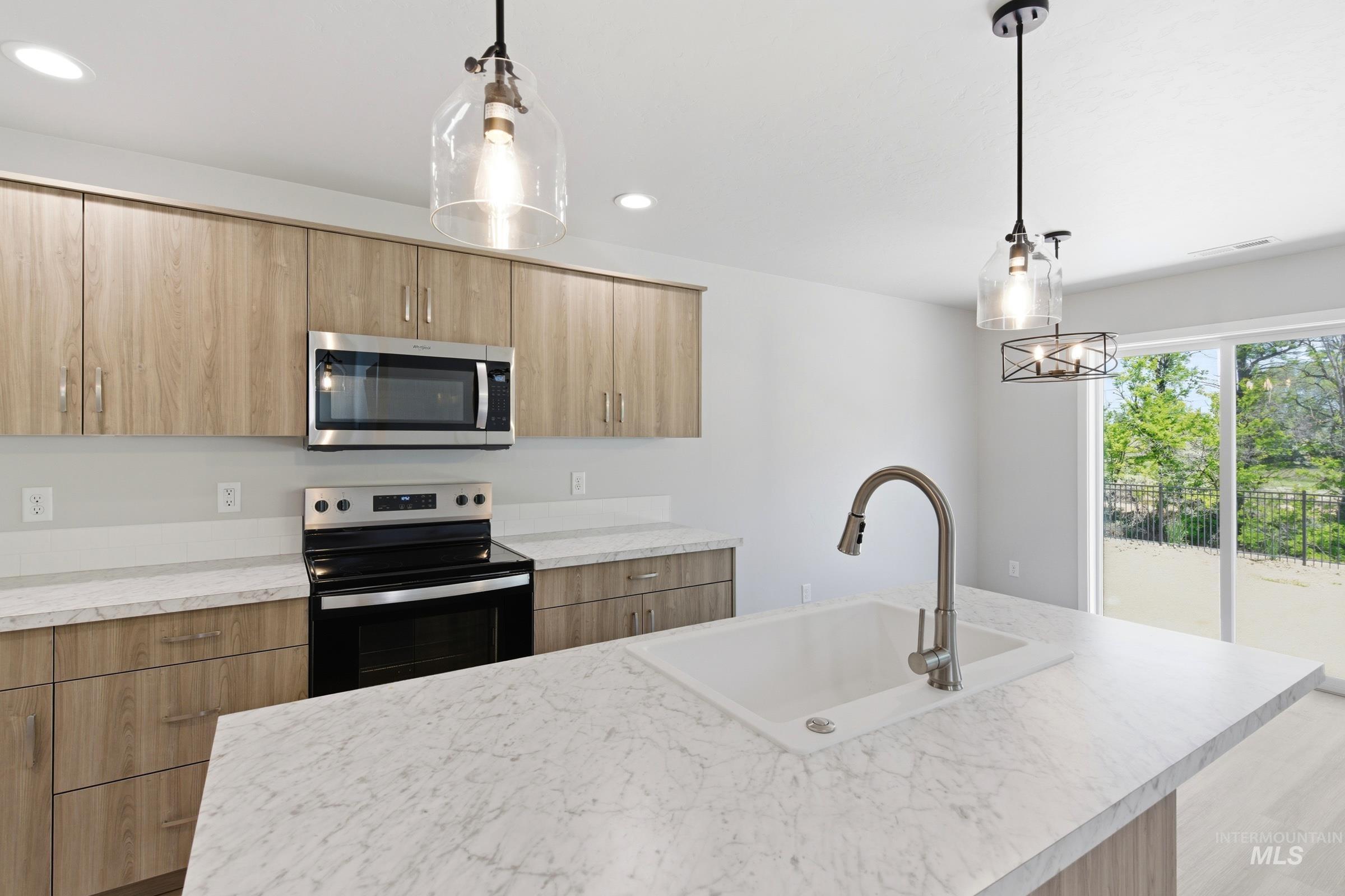 2374 West Fallon Loop Nampa, ID 83651 - Photo 4 of 24 Kitchen featuring an island with an integrated sink and gooseneck faucet, light wood-finish cabinetry, white countertops, and stainless steel appliances