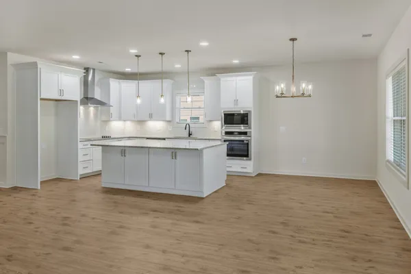 a large kitchen with stainless steel appliances granite countertop a stove a sink a refrigerator and white cabinets with wooden floor