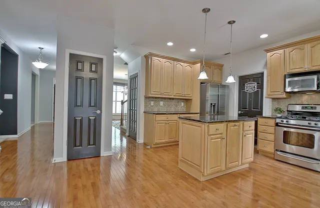 a kitchen with stainless steel appliances granite countertop a refrigerator a sink a stove and oven a wooden floor