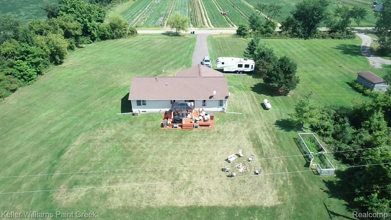 625 Howell Road Allenton, MI 48002 - Photo 41 of 46 Expansive grassy grounds featuring a single-story residence with a brown shingle roof, a rear wood deck, and a gravel driveway
