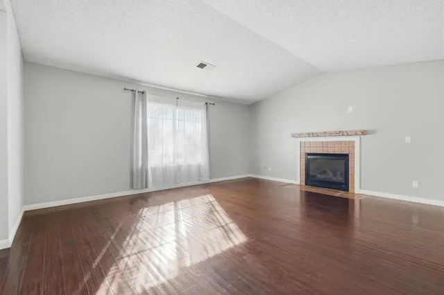 a view of an empty room with wooden floor fireplace and a window