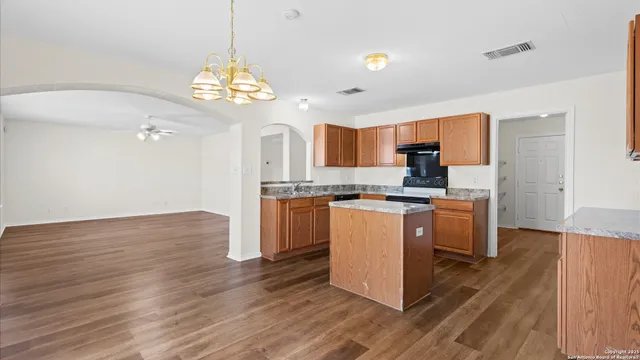 a kitchen with granite countertop a stove top oven a sink dishwasher and a refrigerator with wooden floor