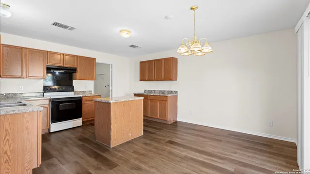 a kitchen with kitchen island granite countertop a stove top oven a sink and dishwasher with wooden floor