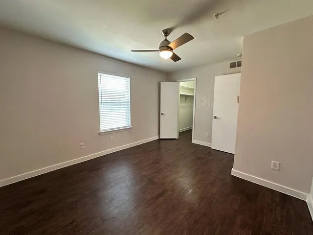 an empty room with wooden floor chandelier fan and windows