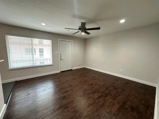 an empty room with wooden floor ceiling fan and windows