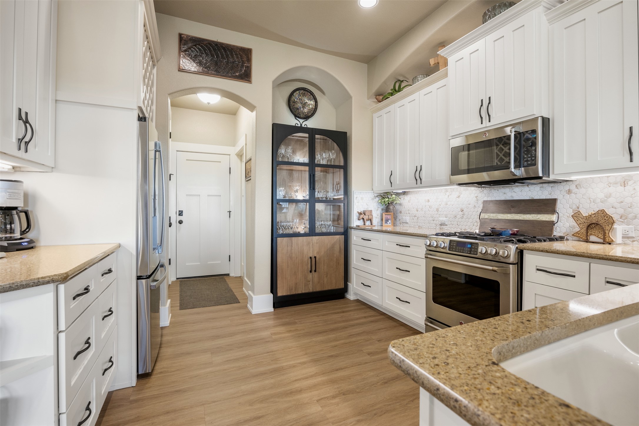 261 Barber Drive Wimberley, TX 78676 - Photo 12 of 37 Kitchen with white cabinetry, stainless steel appliances, arched walkways, light stone counters, and light wood-type flooring