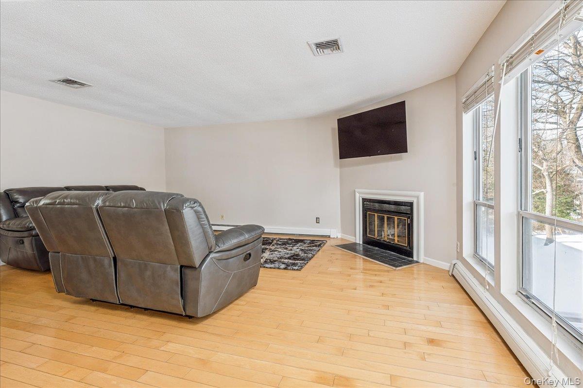58 Villa Drive Peekskill, NY 10566 - Photo 7 of 21 Living room featuring a baseboard heating unit, a fireplace with flush hearth, light wood finished floors, and a textured ceiling
