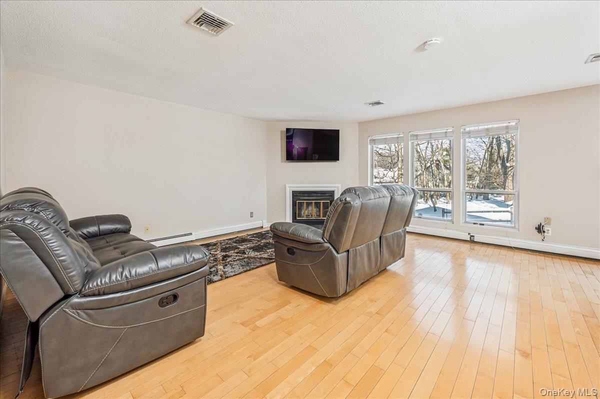 58 Villa Drive Peekskill, NY 10566 - Photo 8 of 21 Living area with a glass covered fireplace, light wood-type flooring, a textured ceiling, and a baseboard radiator